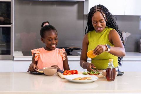 Mother and daughter preparing pancakes together on bright modern kitchen island