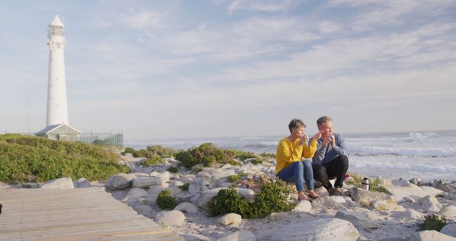 Senior couple enjoying coffee by ocean lighthouse on sunny day - Download Free Stock Images Pikwizard.com