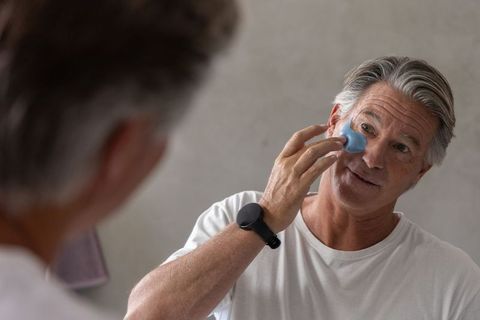 Mature man applying blue under-eye silicone patch during morning grooming and skincare routine