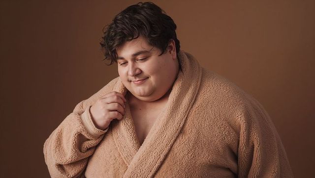 Plus-size man wearing plush tan fleece robe smiling cozy morning self-care portrait warm texture