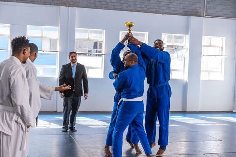 Diverse judo team celebrating victory with gold trophy in training hall