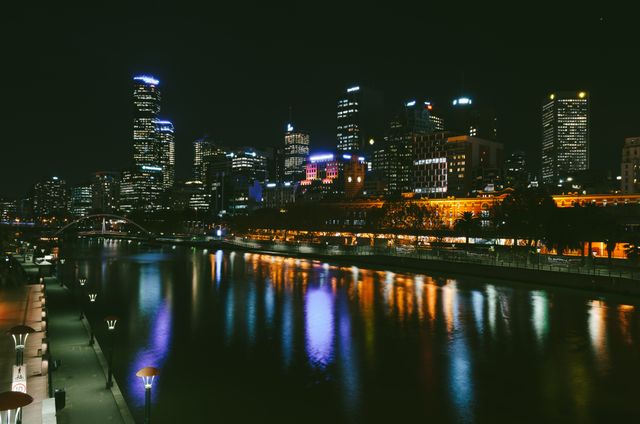 Nighttime cityscape with tall buildings illuminated, reflecting in calm river. Perfect for use in travel brochures, city guides, nightlife promotions, and websites featuring modern urban environments. Ideal for themes related to architecture, city living, and business districts.