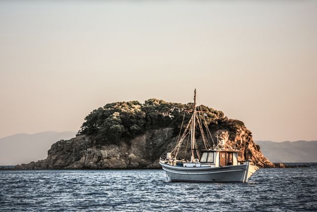 Traditional Wooden Fishing Boat near Rocky Island at Sunset Sea - Download Free Stock Photos Pikwizard.com