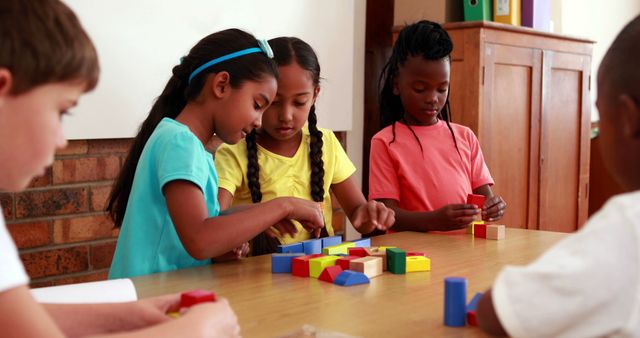 Children are engaging in a collaborative building activity with colorful blocks around a table in a classroom setting. Suitable for educational materials, blog posts about child development, teamwork, classroom dynamics, and early childhood education.