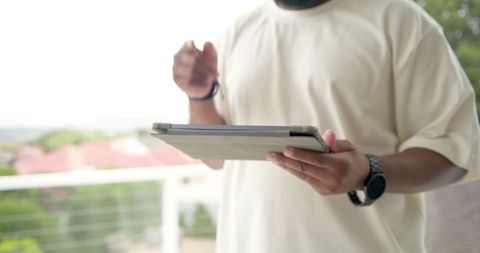 African man holding tablet on balcony wearing oversized tee and wristwatch, urban lifestyle