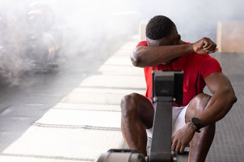 African american man wiping sweat after intense rowing workout on gym rowing machine