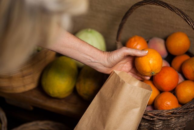 Staff member packing fresh oranges into a paper bag at a supermarket. Ideal for use in articles or advertisements about grocery shopping, organic produce, sustainability, eco-friendly practices, and healthy eating.