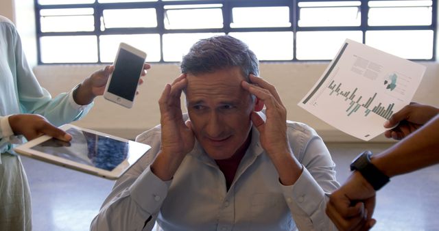 Businessman with hands on head looking stressed as hands hold various digital devices and financial charts. Perfect for illustrating work pressure, technology overload, and multitasking challenges in corporate environments. Suitable for articles on stress management, workplace productivity, and modern work life.