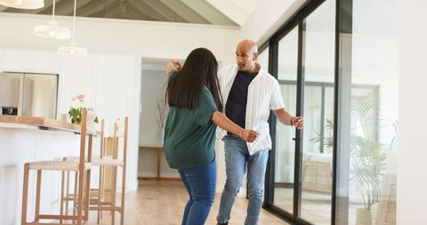 Couple dancing in bright modern open-plan living room on wooden floor by kitchen island