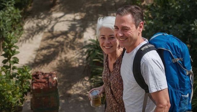 Senior couple smiling while hiking with backpack and travel cup on garden path