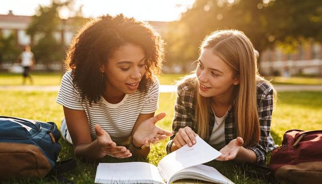 College students studying together on campus lawn discussing textbook during golden hour