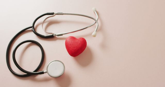 Stethoscope placed next to a red heart symbol on a light pink background. Ideal for illustrating healthcare, medical diagnostics, cardiology services, heart health, medical facilities, and wellness blogs. The combination of doctor’s tool and heart symbol emphasizes the importance of health checkups and medical care.