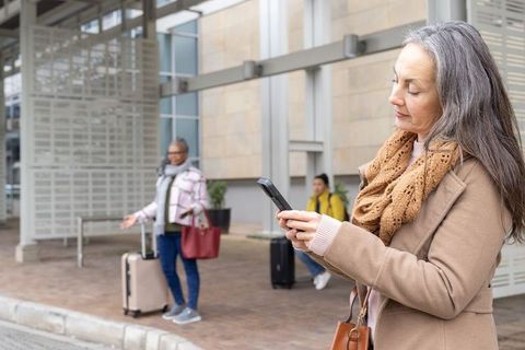 Mature woman checking smartphone while waiting at curbside with diverse travelers