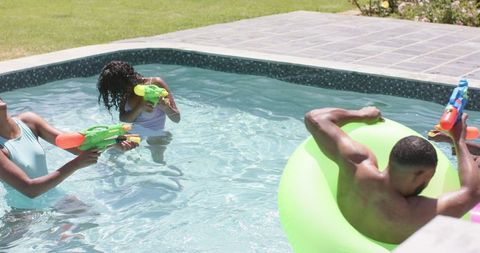 Family enjoying pool activity with water pistols on sunny day