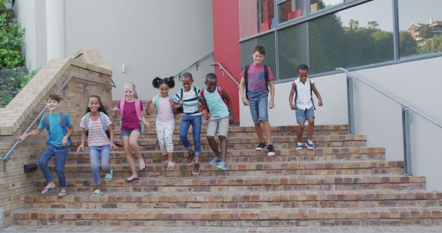 Children joyfully walking down brick stairs outside on a sunny summer day. They carry backpacks, looking cheerful and ready for school activities or summertime fun. Ideal for use in educational materials, advertisements for school supplies, or promoting diversity in children's programs.