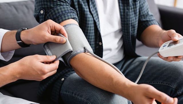 Nurse taking blood pressure on patient arm during home health visit with digital monitor