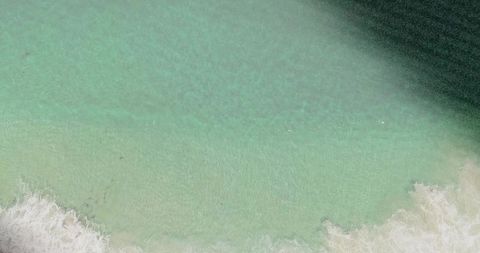 Aerial top-down shallow turquoise coastline revealing sandy beach and reef shadow