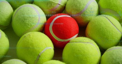 Red tennis ball amidst cluster of vibrant yellow-green balls