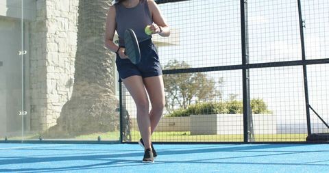 Female athlete playing pickleball on sunny blue outdoor court holding paddle and ball