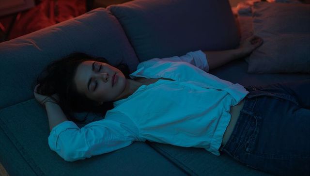 Young woman relaxing on sectional sofa at night in white shirt and jeans, ambient mood