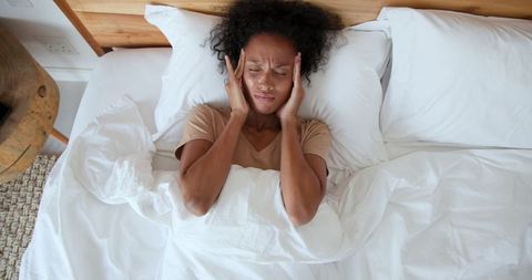Distressed woman lying in bedroom with headache