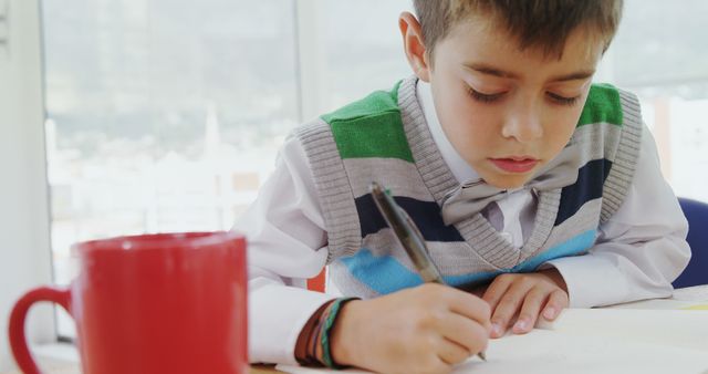 Young Boy Writing with Red Mug on Table in Bright Room - Download Free Stock Images Pikwizard.com