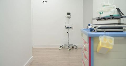 Mobile patient monitor standing in hospital corridor near ct sign with medical supply cart