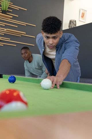 Diverse teen males playing pool in modern game room lining up precision cue shot