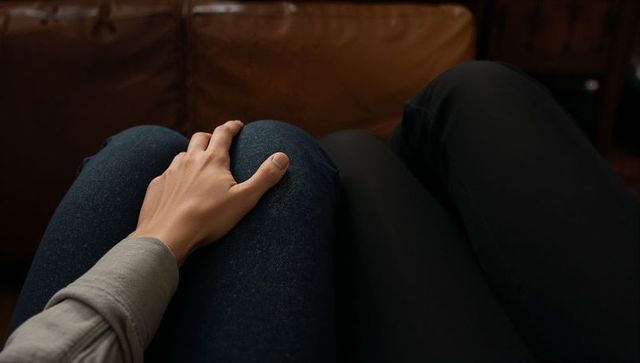 Resting hand on knee conveying intimacy between couple on brown leather sofa