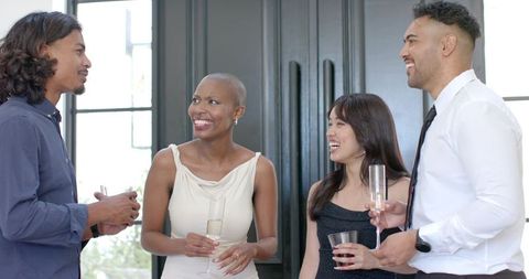 Diverse friends laughing and mingling at elegant reception holding champagne flutes