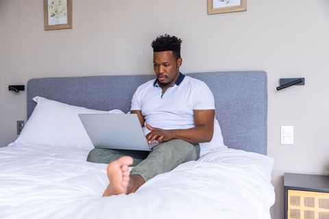 African american man working on laptop in modern minimalist bedroom, remote work and rest
