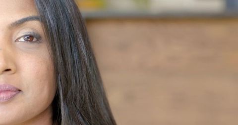 Mid-adult indian woman gazing softly closeup, long hair, warm wood background, copy space