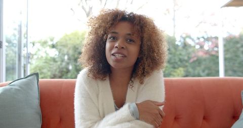Cheerful Woman Relaxing on Orange Sofa During Video Call