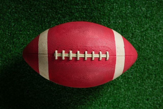 This image shows a close-up view of an American football resting on artificial turf. Ideal for use in sports-related content, advertisements for football gear, or articles about football games and competitions. It can also be used in promotional materials for football events or as a background image for sports websites.