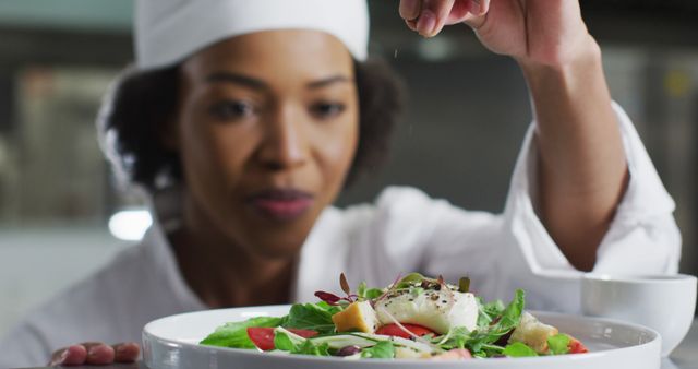 Professional chef meticulously finishing a salad in a restaurant kitchen. Perfect for illustrating culinary expertise, fine dining concepts, and professional food preparation. Useful for articles, menus, blogs, and advertisements focused on high-end gastronomy.