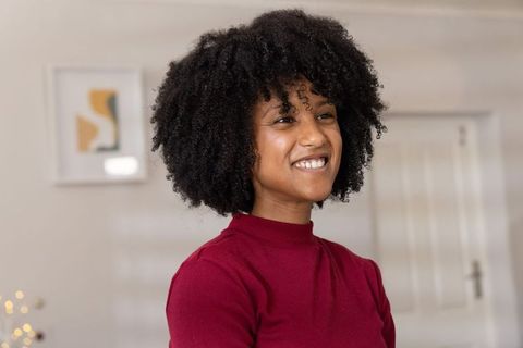 African american woman smiling at home wearing burgundy top, curly hair lifestyle portrait