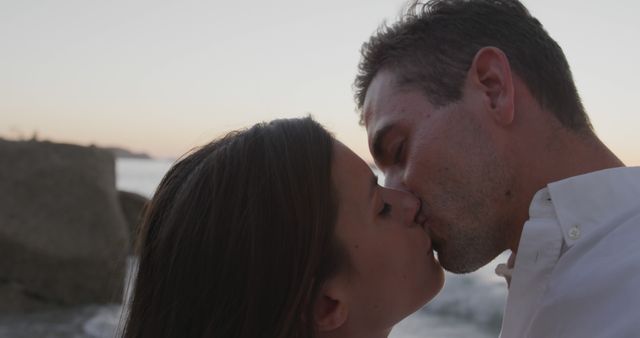 Couple shares intimate kiss on a beach during sunset, highlighting their affection and love. Ideal for use in relationship advice articles, romantic getaway promotions, wedding invitations, or Valentine's Day marketing materials.
