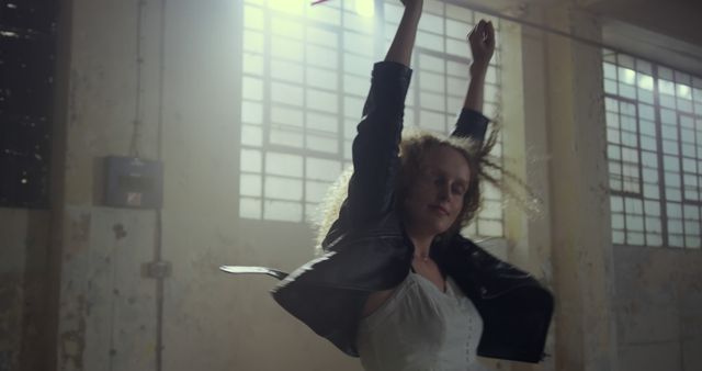 Young Caucasian woman dances passionately in a dimly lit room. Her expressive movement captures the essence of contemporary dance in an indoor setting.