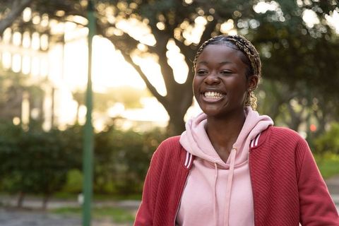 Smiling african american teen walking in park wearing pink hoodie at golden hour