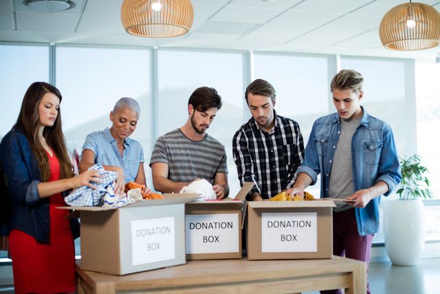 Group of diverse coworkers sorting clothes into donation boxes in a modern office setting. Ideal for illustrating teamwork, corporate social responsibility, charitable activities, and community engagement.