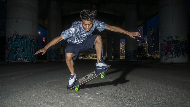 Skateboarder launching midair trick under urban overpass at night with neon wheels and graffiti