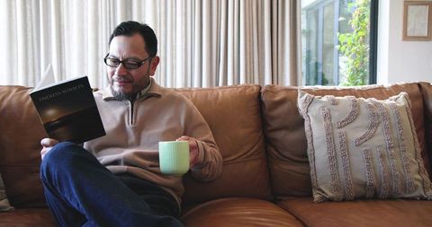 Asian Man Relaxing at Home with Book and Coffee