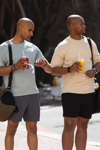 African american friends standing on city street holding cold drinks checking smartwatch