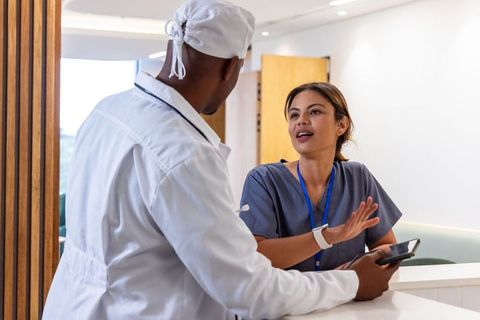 African american doctor and nurse consulting at clinic reception using smartphone