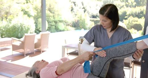 Physical therapist helping senior asian woman with exercise band
