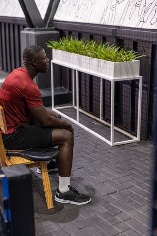 Man resting on bench in modern gym lounge with white planter and wall mural