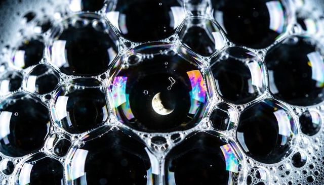 Showing crescent moon reflection inside iridescent soap bubble cluster macro abstract