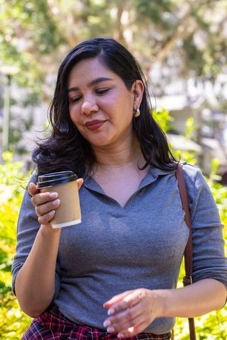 Young woman enjoying takeaway coffee in sunlit urban courtyard wearing red plaid skirt