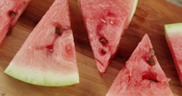 Slices of ripe watermelon are laid out on a wooden cutting board, showcasing their juicy red flesh and black seeds. Watermelon slices like these are often enjoyed as a refreshing snack during warm weather.