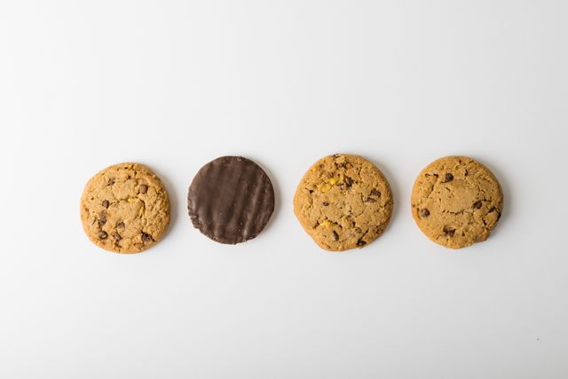 Assorted cookies arranged in a row on a white background, with one chocolate-covered cookie among chocolate chip cookies. Ideal for use in food blogs, dessert recipes, snack advertisements, and bakery promotions. The clean white background provides ample space for text or branding.